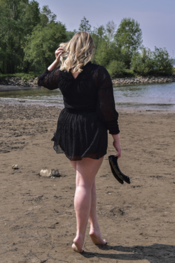 Annika - Escort Model Köln am Strand von hinten im schwarzen Kleid.